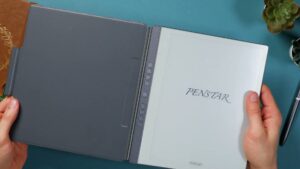 Aufgeklapptes graues Halbfolio links am Penstar eNote; die Tastenleiste liegt zwischen Hülle und Display.