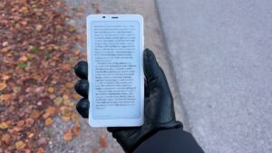 Weißer BOOX Palma 2 mit Buchtext in einer schwarzen behandschuhten Hand im Freien.