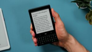 Minimal Phone in einer Hand mit geöffneter englischer Buchseite und vollständig sichtbarer Tastatur.