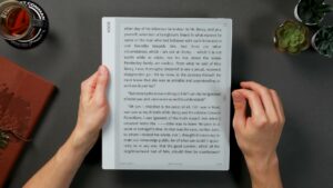 BOOX Note Max mit einer groß gesetzten englischen Romanseite und schmaler Statuszeile, von der linken Hand am Rand gehalten.