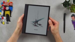 BOOX Note Air 6C in beiden Händen mit breiter linker Griffseite und schwarzem Stift daneben.