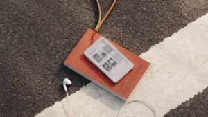 BOOX Picco mit Bibliotheksansicht auf einem Buch neben Kopfhörern und Umhängeband