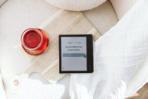 tolino-eReader auf einem Holzbrett neben einem Glas Tee, auf dem Display die Onleihe-Startseite mit „Herzlich Willkommen bei der Onleihe“ und dem Knopf „Bibliothek auswählen“